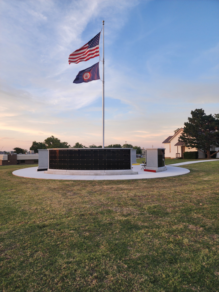 A flag pole flying the American and Citizen Potawatomi Nation flags above the curved walls of the CPN columbarium.