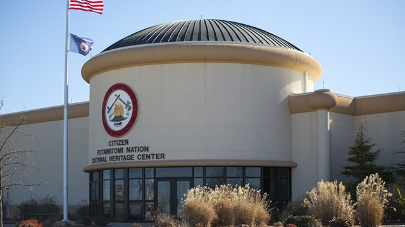 Photo of the front of the CPN Cultural Heritage Center building. An American flag and Citizen Potawatomi Nation flag fly in front of the building.
