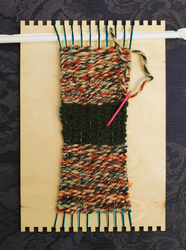 Wooden loom with a small cloth woven out of colored yarn.