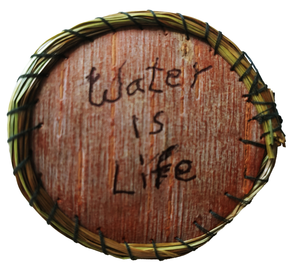 Round wooden disc with a grass border engraved with the words "Water is Life."