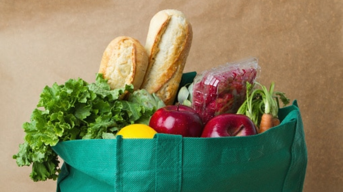Photo of a grocery bag with lettuce, bread, apples, carrots and a lemon.