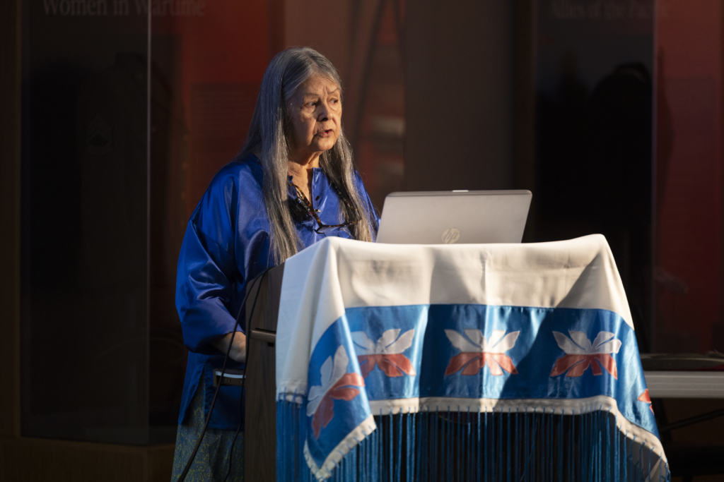 Illuminated at a podium draped with a fringed applique shawl, Minisa Crumbo Halsey speaks about traditional Potawatomi star knowledge.