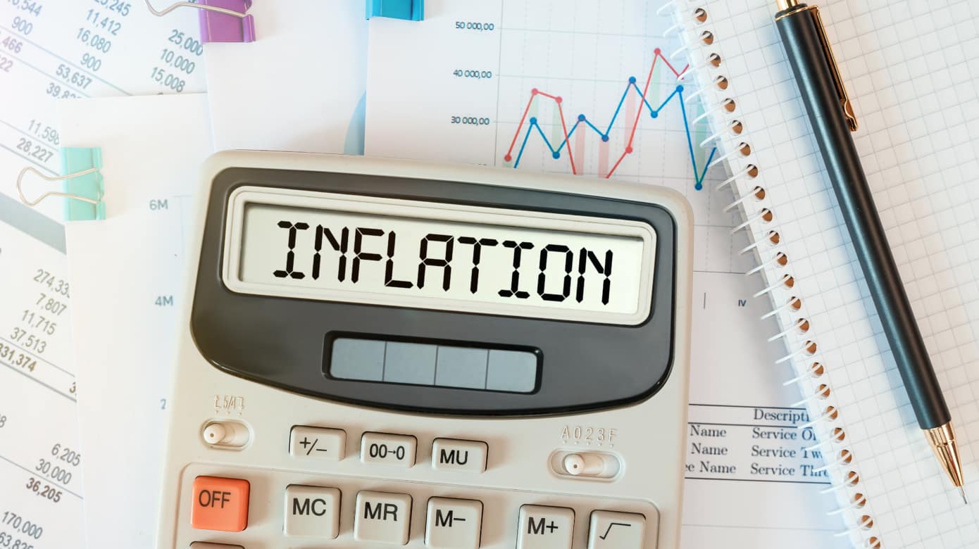 Stock photo of a calculator on top of several pages of charts and numbers. The calculator screen reads "inflation."