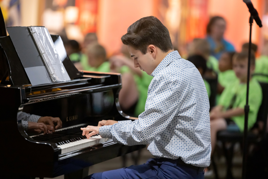 A young student in a blue patterned button down shirt plays a black piano.